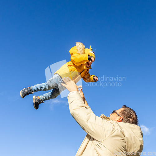 Image of More, more,...dad, that's fun. Happy young father throws his cute little baby boy up in the air. Father's Day, Father and his son baby boy playing and hugging outdoors in nature in fall.