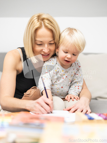 Image of Caring young Caucasian mother and small son drawing painting in notebook at home together. Loving mom or nanny having fun learning and playing with her little 1,5 year old infant baby boy child.