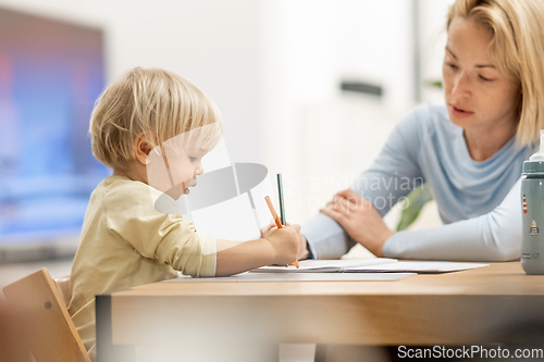 Image of Caring young Caucasian mother and small son drawing painting in notebook at home together. Loving mom or nanny having fun learning and playing with her little 1,5 year old infant baby boy child.