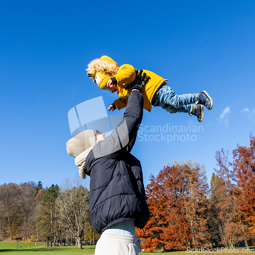 Image of More, more,...mum, that's fun. Happy young mother throws her cute little baby boy up in the air. Mother's Day, Mather and her son baby boy playing and hugging outdoors in nature in fall.