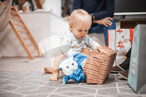 Image of Cute little blond Caucasian toddler unpacking Christmas or Birthday present. Adorable small infant baby boy opening gift