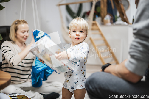 Image of Cute little blond Caucasian toddler unpacking Christmas or Birthday present. Adorable small infant baby boy opening gift