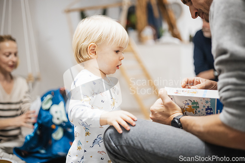 Image of Cute little blond Caucasian toddler unpacking Christmas or Birthday present. Adorable small infant baby boy opening gift