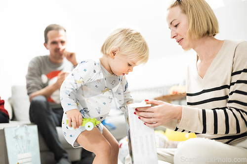 Image of Cute little blond Caucasian toddler unpacking Christmas or Birthday present. Adorable small infant baby boy opening gift.