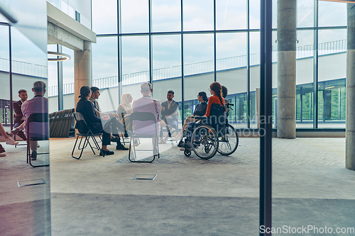 Image of A diverse group of young business entrepreneurs gathered in a circle for a meeting, discussing corporate challenges and innovative solutions within the modern confines of a large corporation