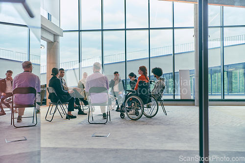 Image of A diverse group of young business entrepreneurs gathered in a circle for a meeting, discussing corporate challenges and innovative solutions within the modern confines of a large corporation