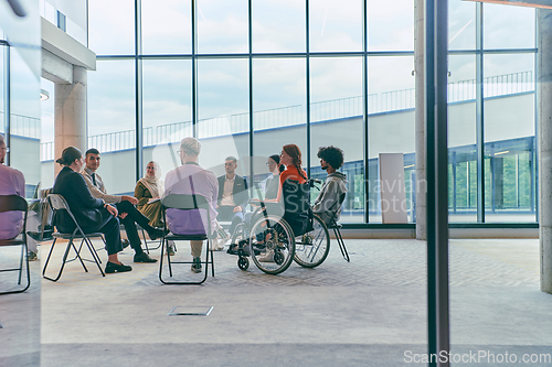 Image of A diverse group of young business entrepreneurs gathered in a circle for a meeting, discussing corporate challenges and innovative solutions within the modern confines of a large corporation