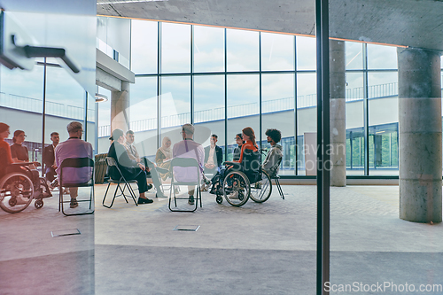 Image of A diverse group of young business entrepreneurs gathered in a circle for a meeting, discussing corporate challenges and innovative solutions within the modern confines of a large corporation