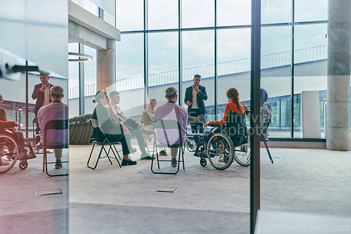 Image of A diverse group of young business entrepreneurs gathered in a circle for a meeting, discussing corporate challenges and innovative solutions within the modern confines of a large corporation