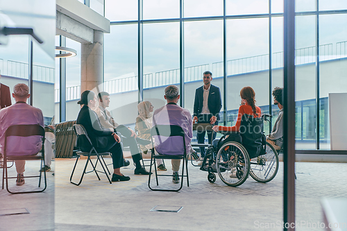 Image of A diverse group of young business entrepreneurs gathered in a circle for a meeting, discussing corporate challenges and innovative solutions within the modern confines of a large corporation