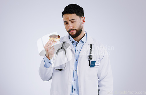 Image of Doctor, diet and thinking with donut in hand for nutrition in studio, white background or mockup space. Nutritionist, choice and man with doubt or decision for health with dessert, sweets or candy