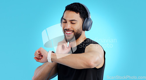 Image of Happy man, headphones and checking watch for pulse in fitness against a blue studio background. Male person, athlete or model looking at wristwatch for monitoring performance or heart rate on mockup