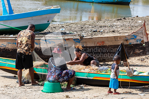 Image of Fisherman and woman repairing fishing nets at the estuaries of a river. The woman has a traditionally Malagasy painted face