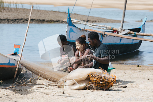 Image of Fisherman and woman repairing fishing nets at the estuaries of a river. The woman has a traditionally Malagasy painted face