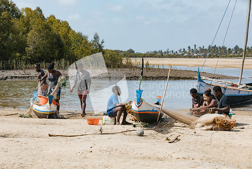 Image of Fisherman and woman repairing fishing nets at the estuaries of a river. The woman has a traditionally Malagasy painted face