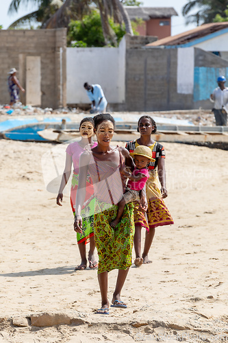 Image of Malagasy woman with her face painted against the sun and a child in her arms walks along the port in Morondava.