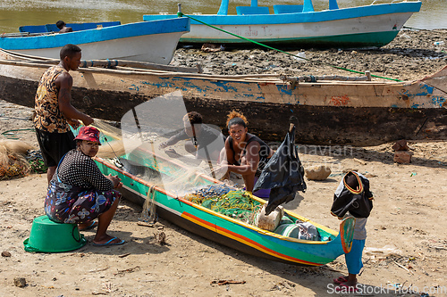 Image of Fisherman and woman repairing fishing nets at the estuaries of a river. The woman has a traditionally Malagasy painted face