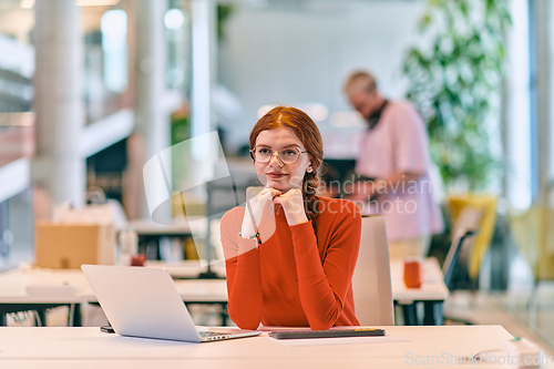 Image of In a modern startup office, a professional businesswoman with orange hair sitting at her laptop, epitomizing innovation and productivity in her contemporary workspace.