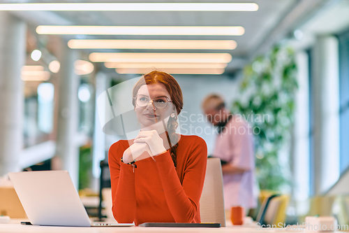 Image of In a modern startup office, a professional businesswoman with orange hair sitting at her laptop, epitomizing innovation and productivity in her contemporary workspace.