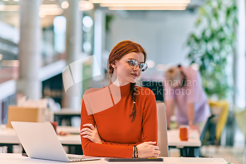 Image of In a modern startup office, a professional businesswoman with orange hair sitting at her laptop, epitomizing innovation and productivity in her contemporary workspace.