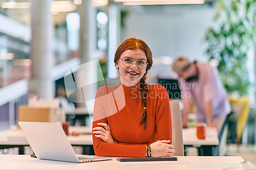 Image of In a modern startup office, a professional businesswoman with orange hair sitting at her laptop, epitomizing innovation and productivity in her contemporary workspace.