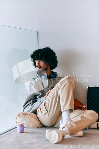 Image of African-American entrepreneur taking a relaxing break from work, sitting on the floor while using wireless headphones and a smartphone for some digital entertainment.