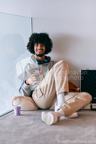 Image of African-American entrepreneur taking a relaxing break from work, sitting on the floor while using wireless headphones and a smartphone for some digital entertainment.