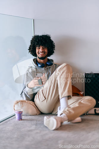 Image of African-American entrepreneur taking a relaxing break from work, sitting on the floor while using wireless headphones and a smartphone for some digital entertainment.