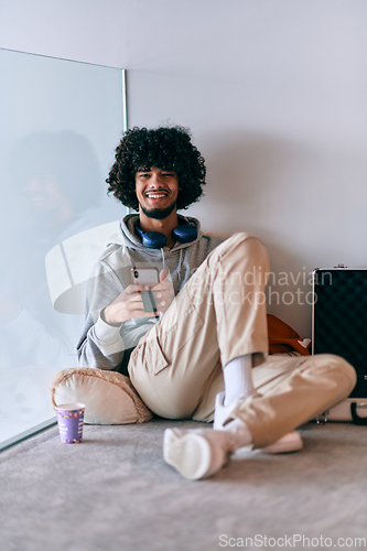 Image of African-American entrepreneur taking a relaxing break from work, sitting on the floor while using wireless headphones and a smartphone for some digital entertainment.