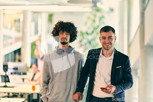 Image of In a modern startup office setting, a business director and a young African American entrepreneur sit surrounded by their colleagues, embodying diversity and teamwork in the corporate world.