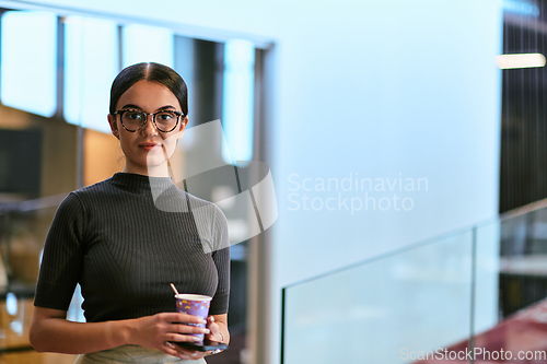 Image of In a bustling modern office a businesswoman in glasses juggles her tasks, sipping coffee and using her smartphone, epitomizing the dynamic and multitasking nature of contemporary corporate life