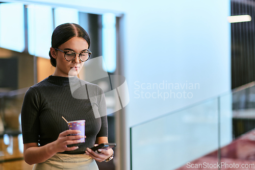 Image of In a bustling modern office a businesswoman in glasses juggles her tasks, sipping coffee and using her smartphone, epitomizing the dynamic and multitasking nature of contemporary corporate life