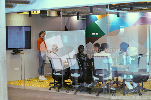 Image of A pregnant business woman with orange hair confidently presents her business plan to colleagues in a modern glass office, embodying entrepreneurship and innovation