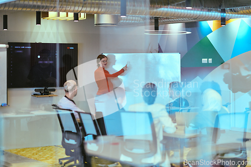 Image of A pregnant business woman with orange hair confidently presents her business plan to colleagues in a modern glass office, embodying entrepreneurship and innovation