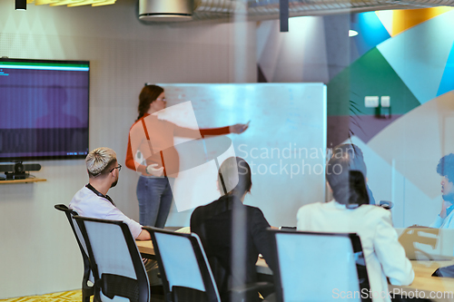 Image of A pregnant business woman with orange hair confidently presents her business plan to colleagues in a modern glass office, embodying entrepreneurship and innovation