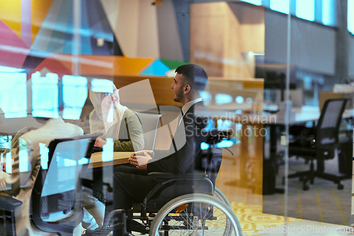 Image of In a modern glass startup office, a wheelchair-bound director leads a successful meeting with colleagues, embodying inclusivity and teamwork.