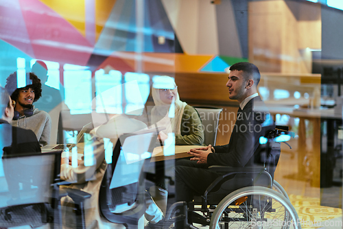 Image of In a modern glass startup office, a wheelchair-bound director leads a successful meeting with colleagues, embodying inclusivity and teamwork.