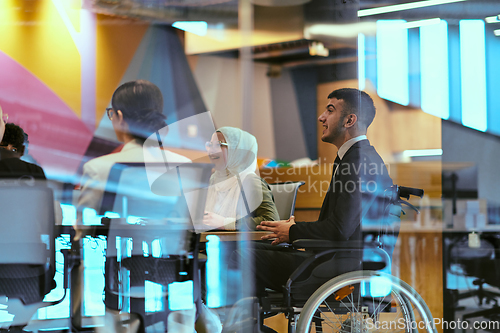 Image of In a modern glass startup office, a wheelchair-bound director leads a successful meeting with colleagues, embodying inclusivity and teamwork.