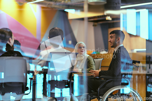 Image of In a modern glass startup office, a wheelchair-bound director leads a successful meeting with colleagues, embodying inclusivity and teamwork.