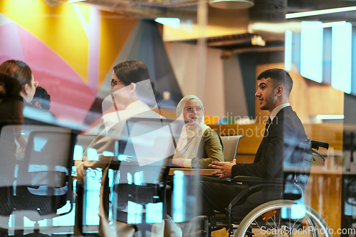 Image of In a modern glass startup office, a wheelchair-bound director leads a successful meeting with colleagues, embodying inclusivity and teamwork.