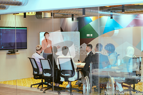 Image of A pregnant business woman with orange hair confidently presents her business plan to colleagues in a modern glass office, embodying entrepreneurship and innovation