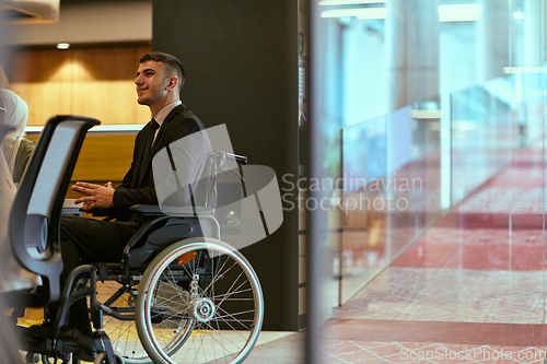 Image of In a modern glass startup office, a wheelchair-bound director leads a successful meeting with colleagues, embodying inclusivity and teamwork.