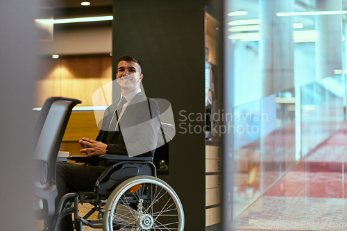 Image of In a modern glass startup office, a wheelchair-bound director leads a successful meeting with colleagues, embodying inclusivity and teamwork.