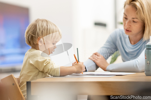 Image of Caring young Caucasian mother and small son drawing painting in notebook at home together. Loving mom or nanny having fun learning and playing with her little 1,5 year old infant baby boy child.