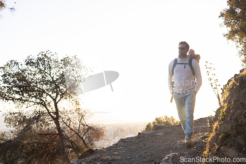 Image of Young father carrying his infant baby boy son in backpack while tracking around Malaga, Spain in sunset. Family travel and vacation concept