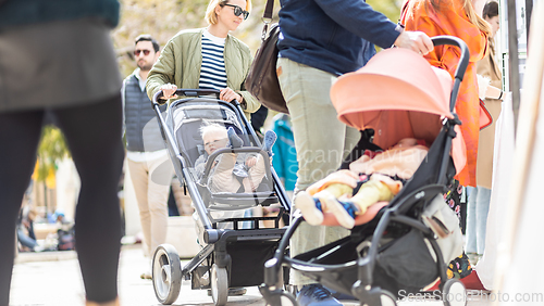 Image of Mother walking and pushing his infant baby boy child in stroller in crowd of people wisiting sunday flea market in Malaga, Spain.