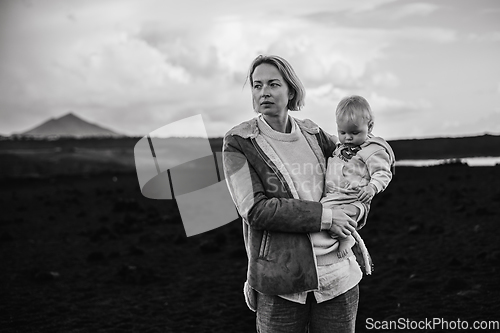 Image of Mother enjoying winter vacations playing with his infant baby boy son on black sandy volcanic beach of Janubio on Lanzarote island, Spain on windy overcast day. Family travel vacations concept.