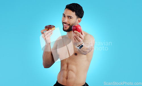 Image of Happy man, portrait and apple with donut for diet, health or nutrition against a blue studio background. Male person or athlete showing natural organic red fruit with chocolate desert on mockup space