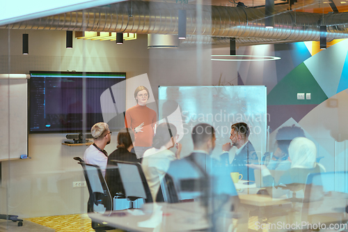 Image of A pregnant business woman with orange hair confidently presents her business plan to colleagues in a modern glass office, embodying entrepreneurship and innovation