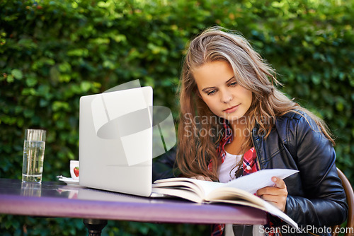 Image of Woman, book and reading for research in cafe, outdoors and sitting for college, work or assignment. Young, female student and technology for online, submission or document by laptop with internet